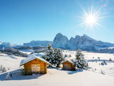 Picturesque landscape with small wooden log cabin on meadow Alpe di Siusi on winter time. Seiser Alm, Dolomites, Italy. Snowy hills with orange larch and Sassolungo and Langkofel mountains group