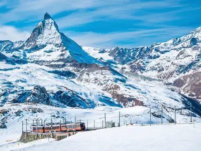 View of red train climbing up to gornergrat station. Scenic view of matterhorn mountain against sky. Famous tourist place in alpine region.