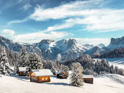 Picturesque landscape with small wooden log cabin on meadow Alpe di Siusi on sunrise time. Seiser Alm, Dolomites, Italy. Snowy hills with orange larch and Sassolungo and Langkofel mountains group