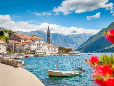Scenic panorama view of the historic town of Perast at famous Bay of Kotor with blooming flowers on a beautiful sunny day with blue sky and clouds in summer, Montenegro, southern Europe