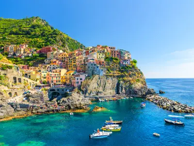Manarola traditional typical Italian village in National park Cinque Terre, colorful multicolored buildings houses on rock cliff, fishing boats on water, blue sky background, La Spezia, Liguria, Italy
