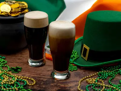 St Patricks day party and Irish celebration of patron saint concept theme with frothy glasses of dry stout, green hat with a buckle, a pot of gold, the flag of Ireland and beads with shamrock in a pub