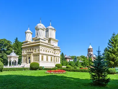 Daylight view to monastery garden park and cathedral on background. Green trees and bushes. Bright blue clear sky. Negative copy space, place for text. Curtea de Arges, Romania