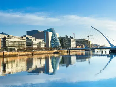 Modern buildings and offices on Liffey river in Dublin on a bright sunny day, bridge on the right is a famous Harp bridge.