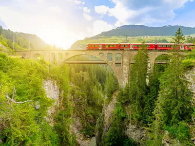 Red train crossing the Solis Viaduct bridge of Swiss railway in Switzerland to Pontresina town. Swiss train Bernina in Grisons at sunset. Albula Railway section between Thusis and Tiefencastel