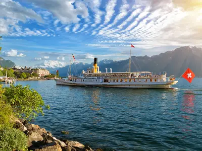 Beautiful summer evening landscape of Lake Geneva with picturesque shores and pleasure ship against Alpine mountains in the rays of the setting sun in Montreux, Switzerland