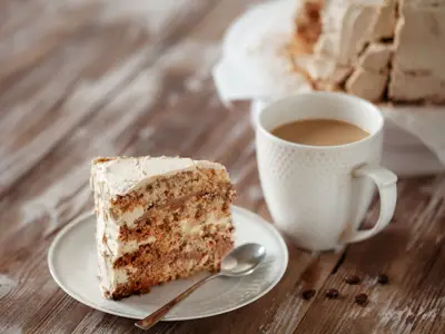 Piece of crispy coffee and nut meringue cake with traditional butter cream frosting on wooden background