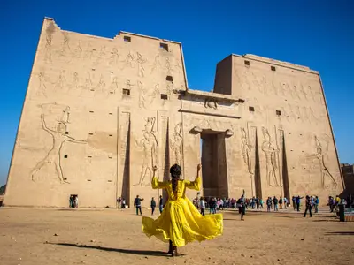 Woman with yellow dress looking at the Temple of Edfu, on a blue sky day, Egypt