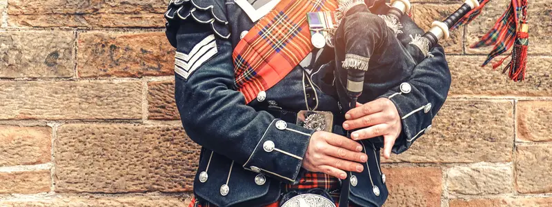 EDINBURGH, SCOTLAND, 24 March 2018 , Scottish bagpiper dressed in traditional red and black tartan dress stand before stone wall. Edinburgh, the most popular tourist city destination in Scotland.