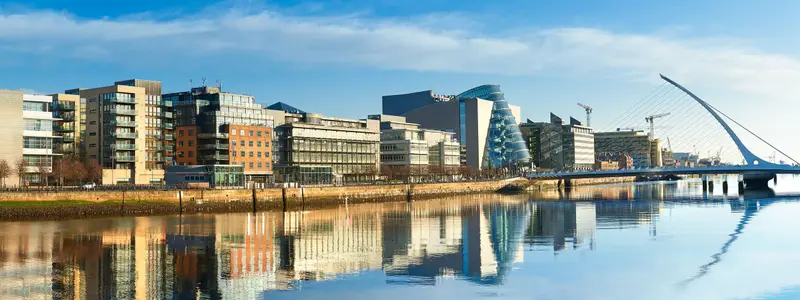 Modern buildings and offices on Liffey river in Dublin on a bright sunny day, bridge on the right is a famous Harp bridge.