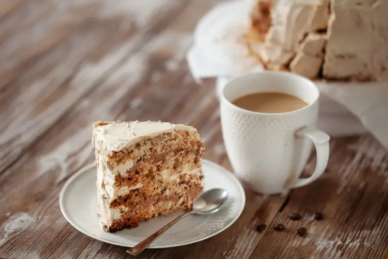 Piece of crispy coffee and nut meringue cake with traditional butter cream frosting on wooden background